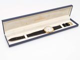 a watch and a pen in a box on a white surface