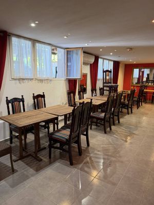 Des tables et des chaises sont alignées dans une grande pièce aux rideaux rouges.