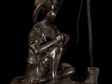 bronze statue of a boy sitting on a rock with a hat on his head