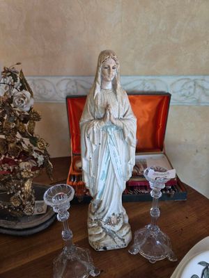 une statue de la Vierge Marie posée sur une table, à côté de verres à vin