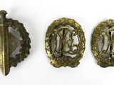 trois insignes en laiton comportant des initiales et une épée sur fond blanc