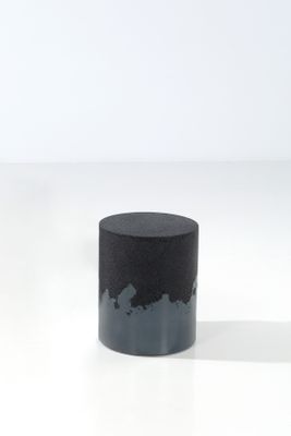 un vase noir posé sur une table blanche, près d'un mur blanc