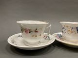 two cups and saucers with floral designs on them sitting on a table