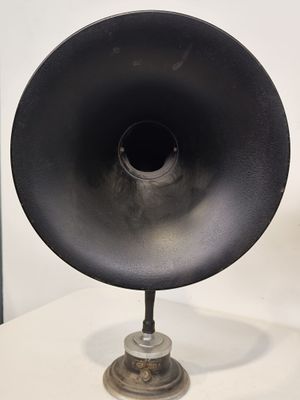 une grande enceinte noire posée sur un pied, sur une table blanche