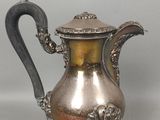 cafetière plaquée argent avec une anse et une cuillère, posée sur un socle