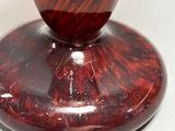 a close up of a red and black vase on a white surface