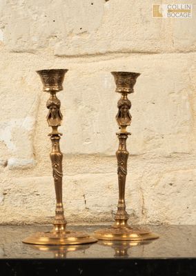 deux bougeoirs en or posés sur une table devant un mur de briques