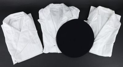 trois paires de pantalons blancs et un chapeau noir posés sur une surface noire