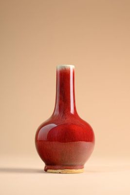un vase rouge posé sur une table, sur fond beige
