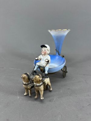une figurine représentant un garçon sur une petite charrette, accompagné de deux chiens