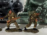 three figurines of men in military uniforms are posed next to a poster