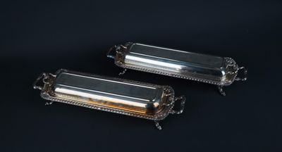 two silverplated rectangular trays with handles on a black background