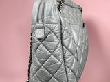 a close up of a grey quilted purse on a pink background