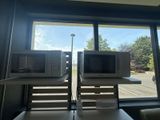 two microwaves that are sitting on a table in front of a window