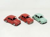 trois petites voitures miniatures sont disposées côte à côte sur une surface blanche