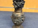 vase en laiton orné d'un visage sur sa base, posé sur un tapis bleu