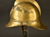 an antique brass helmet on a metal stand against a black background