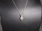 a white gold necklace with a diamond heart pendant on a black mannequin