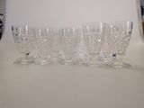 four glasses are lined up on a table with a clock in the background