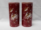 une paire de vases rouges ornés de motifs floraux, posés sur une surface blanche