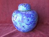 un vase bleu muni d'un couvercle, posé sur un tissu rouge