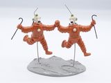 two figurines of clowns are posed on top of a rock