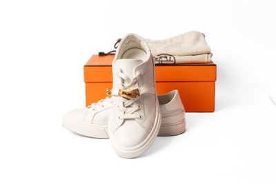 une paire de baskets blanches posée sur une boîte, à côté de deux boîtes orange