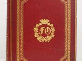 un vieux livre rouge aux tranches dorées, avec un monogramme doré sur la couverture