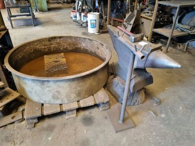 un grand saladier en métal posé sur une palette dans un atelier