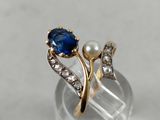 a close up of a ring with a blue stone and a pearl