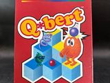 La boîte du jeu vidéo Q-Bert est posée sur la table.