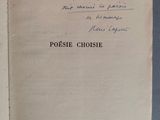 un livre ouvert, sur lequel est inscrit un poème manuscrit, posé sur une table