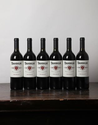 six bottles of red wine are lined up on a table