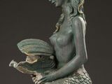 statue of a mermaid reading a book with a shell in her hand
