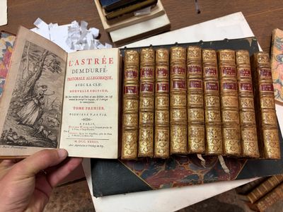 une personne tenant un livre sur lequel sont posés de nombreux autres livres