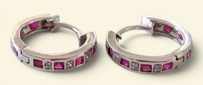 une paire de boucles d'oreilles créoles ornées de diamants roses et blancs sur fond beige
