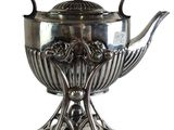 a silver tea pot on a stand with a handle