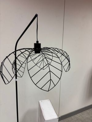 une lampe en métal noir posée sur un pied, à côté d'une boîte blanche