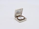 une petite montre de poche posée sur une surface blanche