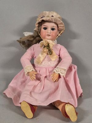 a doll that is sitting on the ground wearing a pink dress and hat