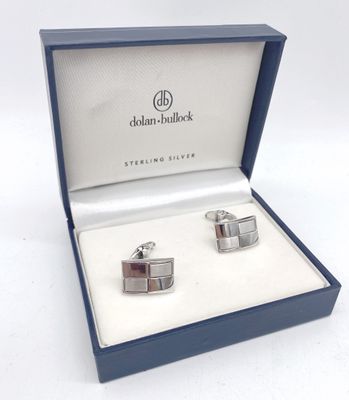 deux boutons de manchette en argent dans un coffret bleu sur fond blanc