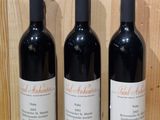 three bottles of red wine sit on a shelf in front of a wooden wall