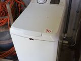 une machine à laver blanche posée dans un garage, à côté d'un tas de pneus