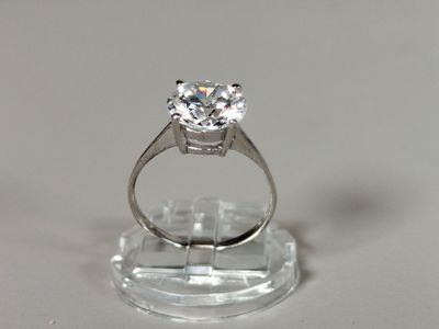 une photo d'une bague en diamant posée sur un socle transparent, sur une surface blanche