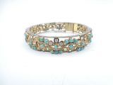 a close up of a gold and turquoise bracelet on a white surface