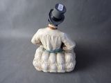 a figurine of a woman sitting on a pillow with a hat on top of her head