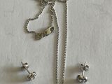 Ensemble collier et boucles d'oreilles en argent posé sur un fond blanc