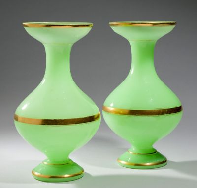une paire de vases en verre vert aux bords dorés, posés sur une surface blanche
