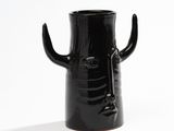 a black vase with a face on it on a white surface