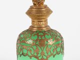 une bouteille en verre verte et dorée, avec un bouchon doré, posée sur une surface blanche